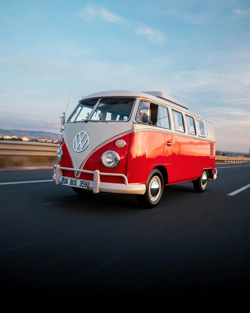 A vintage red and white Volkswagen camper van on a scenic highway